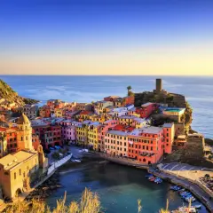 Coloratissimi borghi sul mare aggrappati alla scogliera, con il sole che illumina le case e il blu intenso del mare.