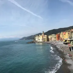 Un angolo di **mare vicino Milano**, con case colorate affacciate su una spiaggia di ciottoli e gente che prende il sole.