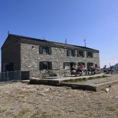 Rifugio in pietra con persone sedute ai tavoli all'esterno, un luogo ideale per una pausa durante un'escursione nei rifugi Emilia Romagna.