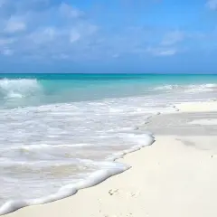 Onda che lambisce la sabbia bianca di una spiaggia d'inverno, con cielo azzurro e nuvole sparse.