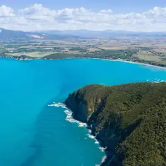 Vista aerea della costa degli Etruschi con mare azzurro, scogliere verdi e un borgo storico.