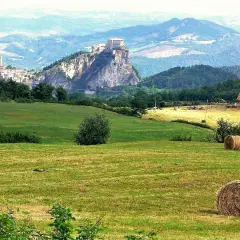 Colline romagnole dove andare: un borgo arroccato su uno sperone roccioso, campi verdi e balle di fieno.