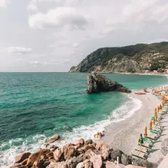 Spiagge libere Liguria: mare turchese, scogli imponenti e file di ombrelloni colorati su una spiaggia di ciottoli.
