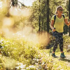 Giovane donna con bastoncini da trekking si gode le sue passeggiate Trentino in un bosco soleggiato.