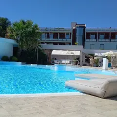 Piscina azzurra e lettini prendisole in un resort, con un edificio moderno sullo sfondo. Un'oasi di benessere e relax, perfetta per godersi le terme Viterbo Salus.