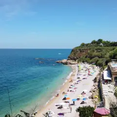 Spiaggia affollata con ombrelloni colorati, mare azzurro e scogliere verdi in Abruzzo. Un resort con piscina domina la scena.