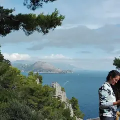 Donna con sciarpa guarda il cellulare, con vista mare e montagne di Capri a piedi.