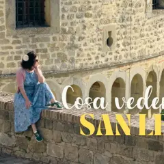 Donna seduta su un muretto di pietra a San Leo, con testo "Cosa vedere a San Leo".
