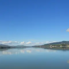 Lago calmo con riflessi di colline verdi e cielo azzurro. Un'ottima meta per scoprire cosa vedere vicino Matera.