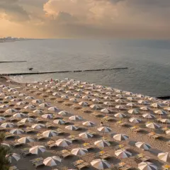 Filetto di sabbia dorata con file ordinate di ombrelloni e lettini, bagnato dal mare del Friuli Venezia Giulia al tramonto.