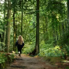 Una ragazza con lunghi capelli biondi sta camminando nei boschi, immersa nella lussureggiante vegetazione verde.