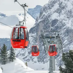 Cabine rosse su un impianto di risalita in Trentino, perfette per esplorare le località sciistiche economiche. Montagne innevate e pini sullo sfondo.