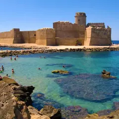 Castello Aragonese su una delle migliori spiagge calabria, con acque cristalline e bagnanti che si godono il sole.