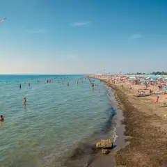 Gente in acqua e sulla sabbia, ombrelloni colorati e gabbiani in volo sulle spiagge friulane.