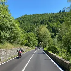 Motociclisti sfrecciano su strade panoramiche dell'Emilia Romagna, tra colline verdi e cielo azzurro.