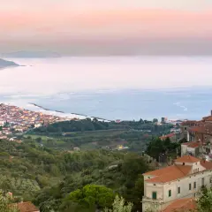 Vista panoramica di un borgo costiero nel Cilento, con case arroccate su una collina che scende verso il mare azzurro.