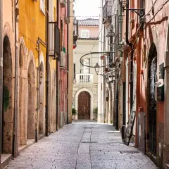 Un vicolo stretto nel chia centro storico, con edifici colorati, archi in pietra e un'antica porta in legno in fondo.