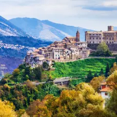 Borgo medievale su una collina verde, con montagne sullo sfondo. Un gioiello di montagna vicino Roma, con case antiche e un castello imponente.