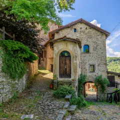 Un vicolo lastricato conduce a un antico portone in legno. La scola di pietra, con edera rampicante, sembra uscita da un libro di fiabe.