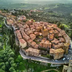 Vista aerea del borgo Panicale in Umbria, con le sue case in pietra e tetti rossi che si aggrappano alla collina, circondato da verdi colline.