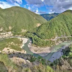 Un fiume serpeggia tra montagne verdi e scoscese, con una strada che costeggia il corso d'acqua. Il borgo di Brugnello si intravede tra la vegetazione lussureggiante.