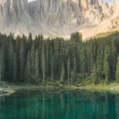 Lago alpino con riflessi di bosco di conifere e montagne imponenti. Un luogo ideale per lo sport e natura.