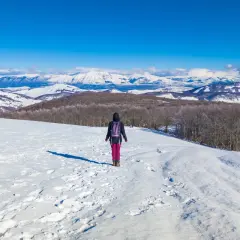 Escursionista in un paesaggio innevato, ideale per scoprire dove andare sulla neve vicino Roma. Montagne imbiancate all'orizzonte.