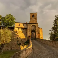 Antica porta di Montegridolfo cosa vedere: un borgo medievale con torre campanaria e vicoli acciottolati, immerso nel verde.
