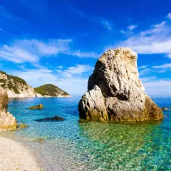 Scogliera imponente su una spiaggia di ciottoli, mare cristallino e isole verdi all'orizzonte. Una splendida località di mare tra Lazio e Toscana.