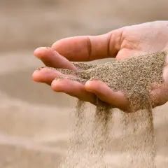 Mano che lascia cadere sabbia bianca, come il tempo che scorre via.