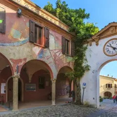 Un arco con orologio conduce a una strada acciottolata, un invito a scoprire i borghi da visitare vicino a Forlì.