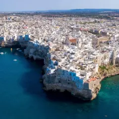 Vista aerea di Polignano a Mare, con le case bianche a picco sul mare blu intenso. Un gioiello della Valle d'Itria, dove il mare incontra la terra.