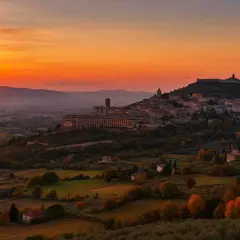 Tramonto infuocato su una città dell'Umbria arroccata su una collina, con uliveti e campi dorati.