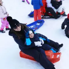 Mamma e bambino felici sciano in Abruzzo con slittino. Altri bambini giocano sulla neve.