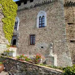Antica dimora a Compiano, Parma, con mura in pietra, edera rampicante, fiori e una statua.