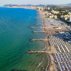 Vista aerea di una spiaggia affollata con ombrelloni colorati e il mare azzurro, tipica di una città riviera romagnola.