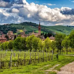 Due escursioniste passeggiano tra vigneti rigogliosi e dolci colline modenesi, con un borgo antico sullo sfondo.