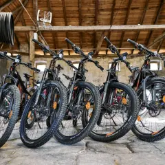 Bici in montagna pronte per l'avventura. Diverse mountain bike nere con dettagli arancioni, parcheggiate in un fienile con travi in legno.
