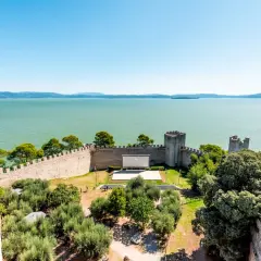 Vista dall'alto di un castello con un cinema all'aperto, circondato da ulivi e affacciato sul lago Trasimeno, uno dei borghi vicino Castiglione del Lago.
