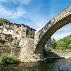 Antico ponte in pietra a schiena d'asino, con case aggrappate alla collina. Un scorcio suggestivo del portico di Romagna.