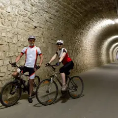 Coppia in bicicletta nel tunnel del **parenzana tracciato**, un percorso suggestivo tra storia e natura.