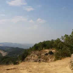 Croce in cima a un crinale roccioso, con vista panoramica sui monti dell'Emilia Romagna e un cielo azzurro con nuvole bianche.