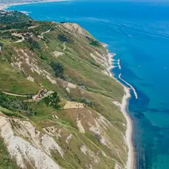 Vista aerea del **lungomare Rimini** con colline verdi, case sparse e il mare azzurro.