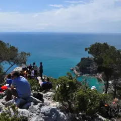 Gruppo di persone in pausa durante un trekking a Finale Ligure, con vista sul mare azzurro e scogliere.