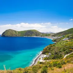 Splendido mare di Lipari con acque cristalline che lambiscono una costa verdeggiante e un borgo bianco.