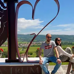 Co zobaczyć w Valpolicella: para siedzi na ławce przed rzeźbą serca i postacią, z widokiem na winnice i wzgórza.