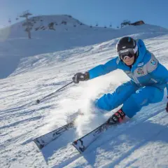 Sciatore in azione su una pista innevata, tipica delle località sciistiche Piemonte, con sole splendente e skilift sullo sfondo.