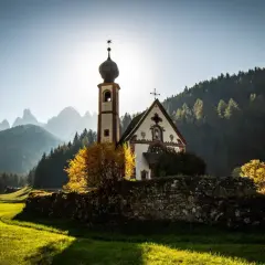 Chiesa di San Giovanni in Ranui, incastonata nel **Val di Funes**, con le Dolomiti sullo sfondo illuminate dal sole.
