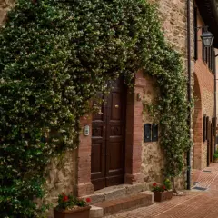 Un antico borgo in Umbria, con un portone di legno scuro avvolto da rampicanti fioriti. La strada in mattoni rossi sale dolcemente tra case in pietra.