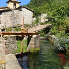 Un canale d'acqua cristallina attraversa un borgo antico, ricordando la Venezia dell'Umbria. Edifici in pietra e vegetazione rigogliosa incorniciano questo scorcio pittoresco.